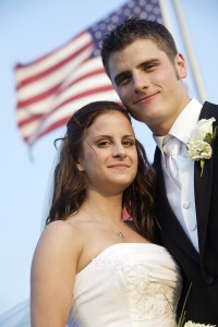 Bride and grrom standing in front of american flag.