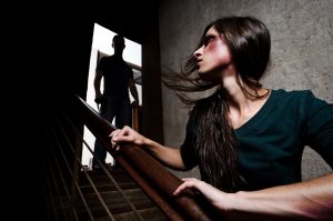 Battered woman escaping from man silhouetted at the top of the stairs, in fear of more violence