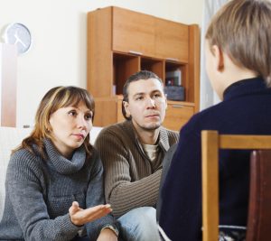 Parents talking to teenager in living room.