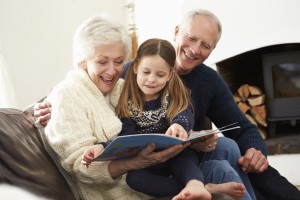Grandparents And Granddaughter Reading Book At Home Together