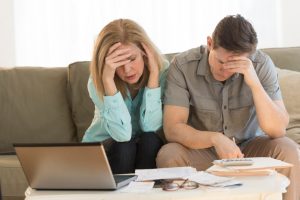 Worried mature couple calculating home finances on sofa